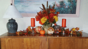 A Fall Collection used on a table top with a pumpkin, cat tails, candles and dried flowers