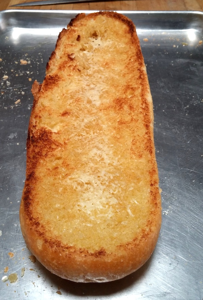 A half loaf of golden toasted garlic bread sitting on an aluminum cookie sheet.
