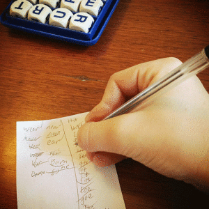 A hand with pen writing words on paper, playing boggle.