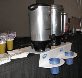 Two aluminum coffee pots sitting on white original drip catchers at a banquet.