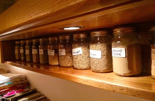 Long oak spice shelf with jars of spices on it.