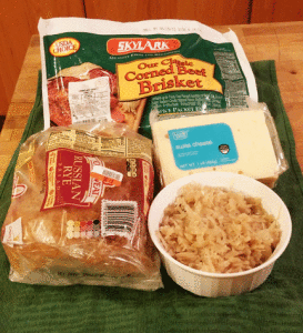 reuben sandwich ingredients laid out on a counter, including corned beef, rye bread, swiss cheese and sauerkraut.