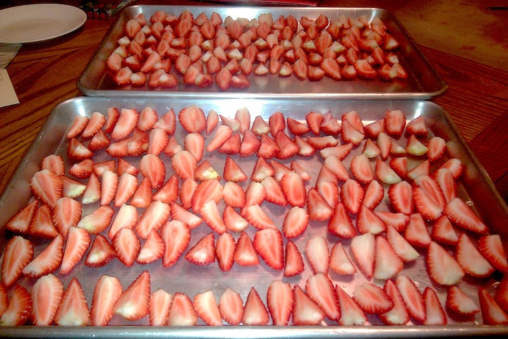 Strawberries cut in quarters and laid out on a cookie sheet to be frozen.