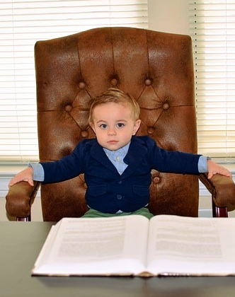 young boy sitting at a large business desk with a book opened in front of him