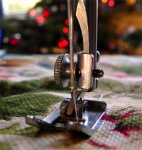 A sewing machine foot with white bobbin thread coming up from the bottom.