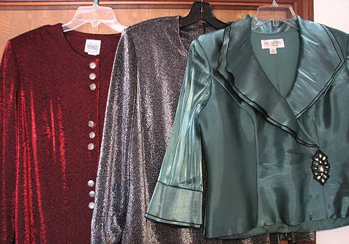 3 sparkly holiday blouses—red, silver and green, hanging on hangers.