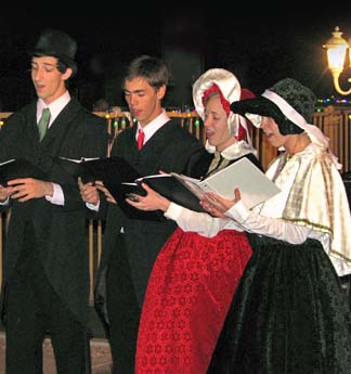 Fun Family Christmas Traditions: 9 Exciting and Inexpensive Holiday Activities 2 Four Christmas carolers (2 guys and 2 girls) singing at a local resort.