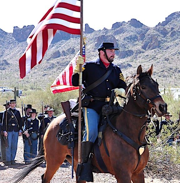 A Civil War reinactment in arizona a soldier on a horse carrying an American Flag.