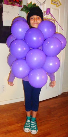 A girl with purple balloons on her body, dressed as a cluster of grapes.