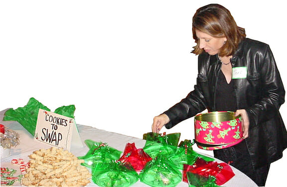 A woman walking around a table filled with holiday cookies