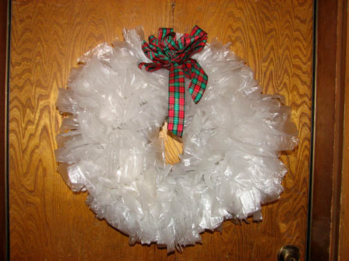A Christmas Crafted plastic grocery bag wreath on an oak door.