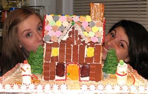 Fun Family Christmas Traditions: 9 Exciting and Inexpensive Holiday Activities 3 Two girls peeking out from behind a small gingerbread house.
