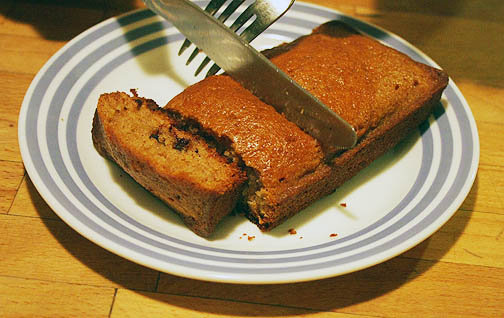 IMG_9973Cutting-Sample-Loaf-Zucchini-Bread-Small (1) A silver knife and fork being used to cut a loaf of chocolate chip zucchini bread. A delicious snack for kids.