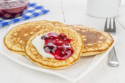 3 pancakes on a white plate with cherry and blueberry topping.