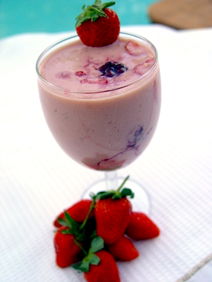 A smoothie in a tall stemmed glass with strawberries on it.
