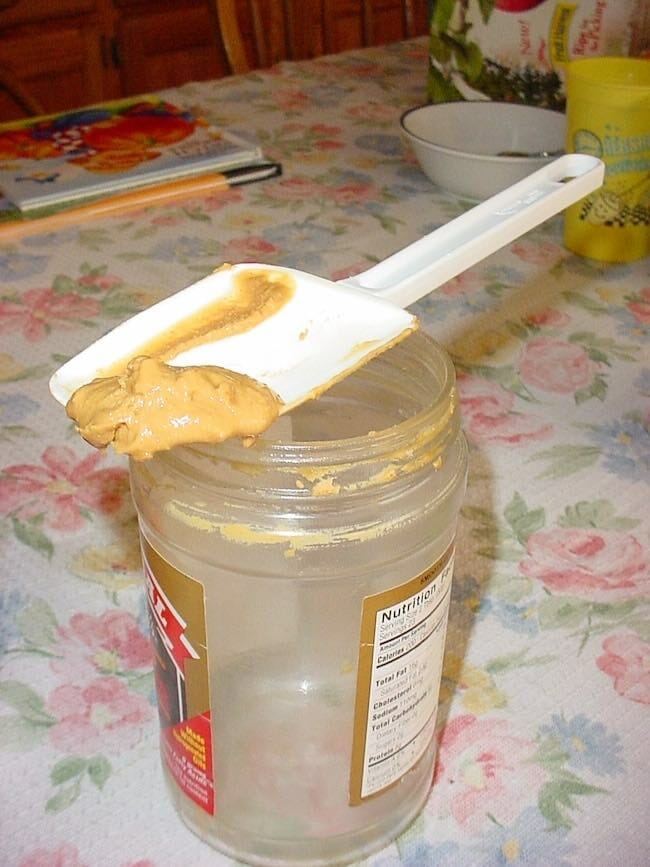 A spoonula used to clean out a peanut butter jar.