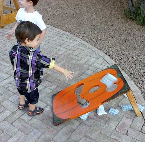 DIY Halloween Party Games, Crafts & Food Ideas for Fun Harvest Festival 4 Grandson Jason tossing a bean bag through the Jack-O-Lantern while grandson Stark waits for his turn.