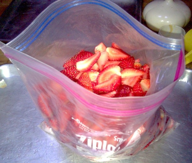 Save Money on Fruits & Veggies - Produce Savings 7 Cut-up frozen strawberries are put into a zippered plastic bag ready to be stored in the freezer.