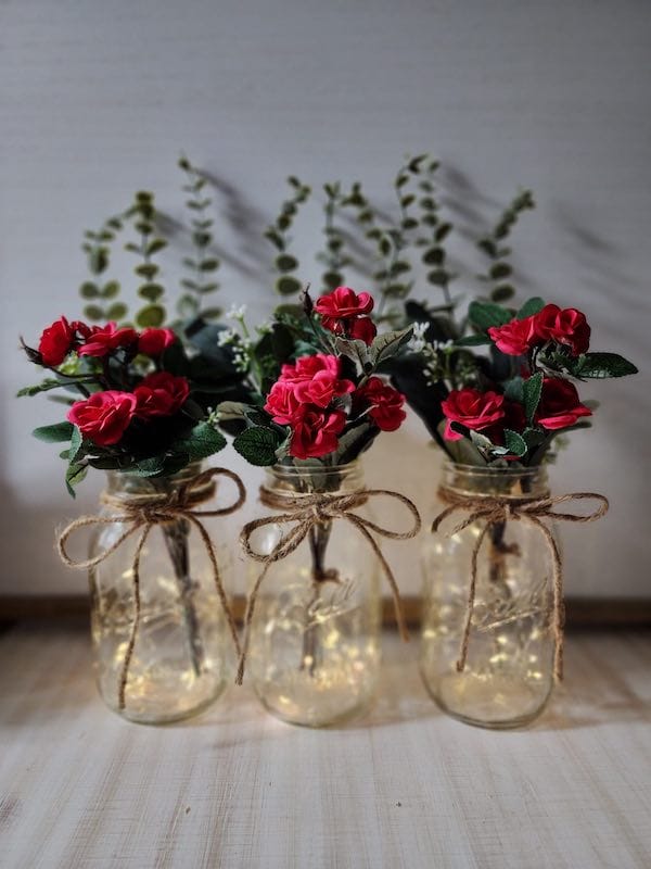 Mason jars with red roses and fairy lights.