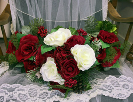 A bridal bouquet full of red and white roses sitting on a brides veil.
