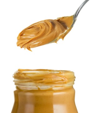 A tablespoon of peanut butter coming out of a jar.