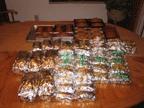 Many loaves of Christmas pumpkin bread wrapped in silver aluminum foil, stacked on a kitchen table.