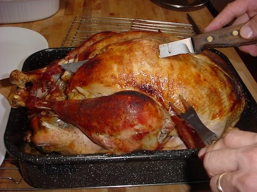 A man carving a cooked turkey with a long, sharp knife and meat fork.