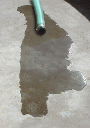 A green hose leaking water on concrete.