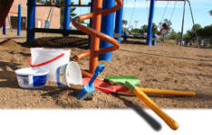 Plastic rake and shovel with two white buckets in the sand of a playground.