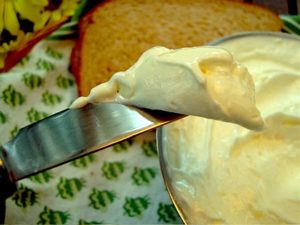 A butter knife with spreadable butter on it with a piece of bread below it. 
